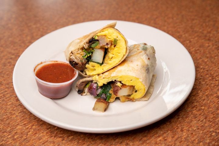 A breakfast burrito cut in half with a cup of salsa